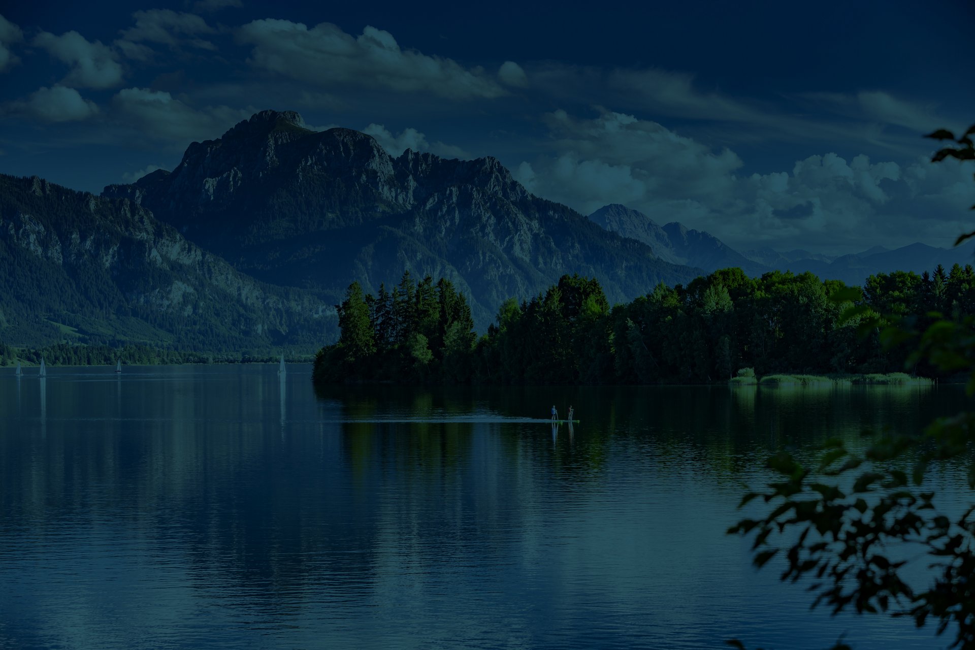 Landschaftsaufnahme des Forggensees in der Nähe von Füssen. Im Hintergrund ist ein wunderschönes Bergpanorama zu sehen.